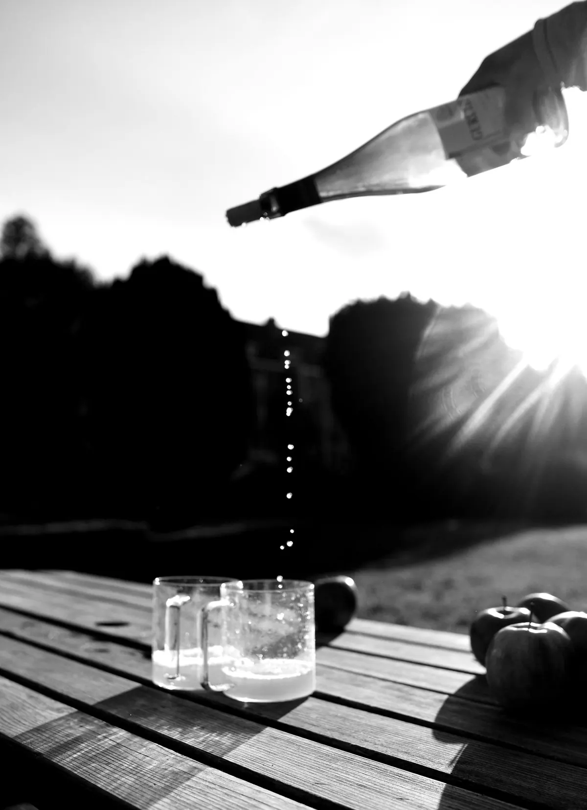 Basque cider poured from a height into glasses on a wooden table, backlit by the sun